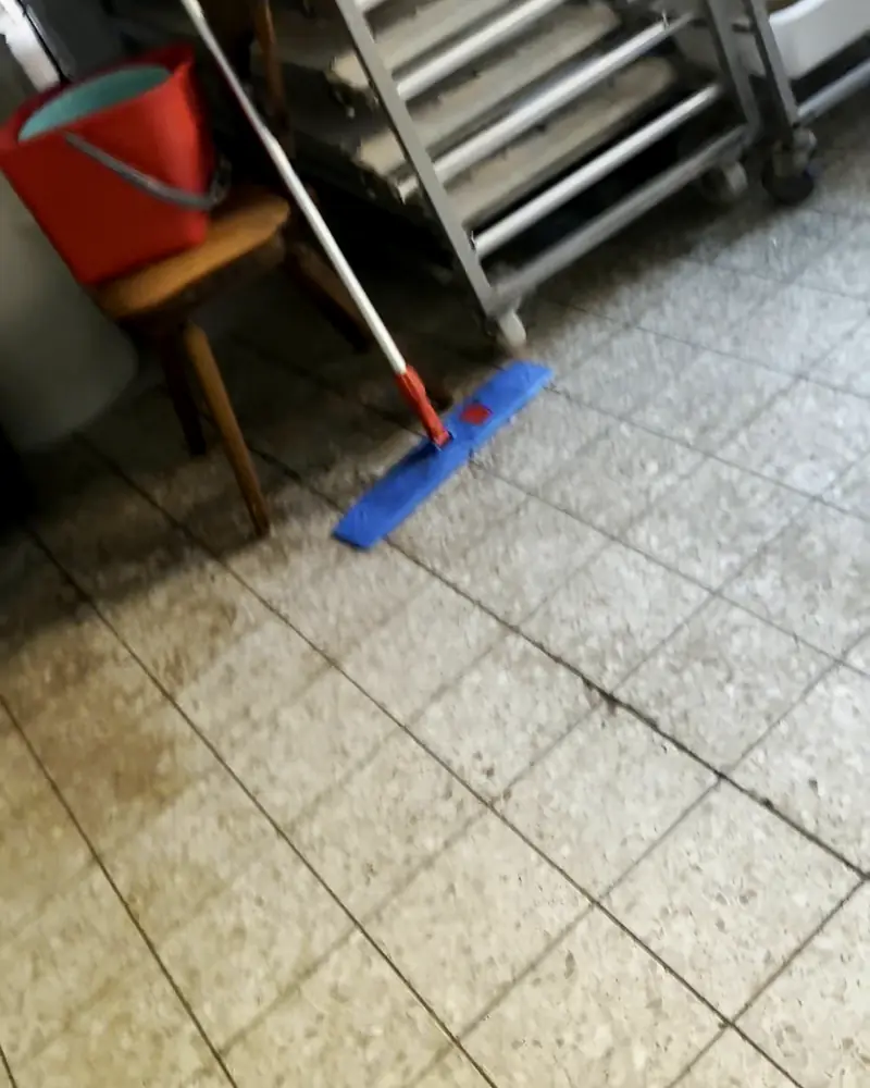 Küchenboden mit Flecken und verschmutzten Fugen neben einem Regalwagen